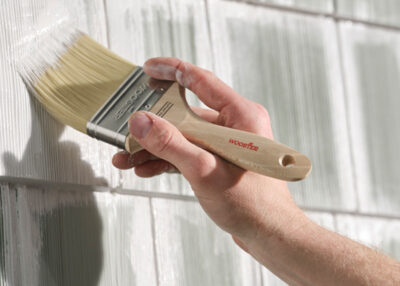 close up of a man painting an exterior wall white with a paintbrush