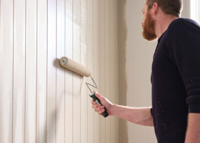 man paints a wall white with a paint roller